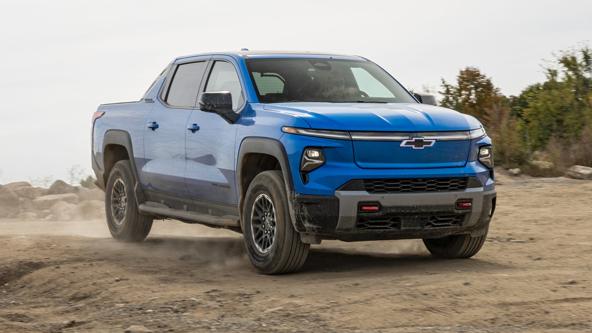 Chevrolet Silverado EV Trail Boss Off-Road Prowess A Chevrolet Silverado EV Trail Boss parked on a dirt trail, showcasing its large tires and robust stance, highlighting its off-road prowess.