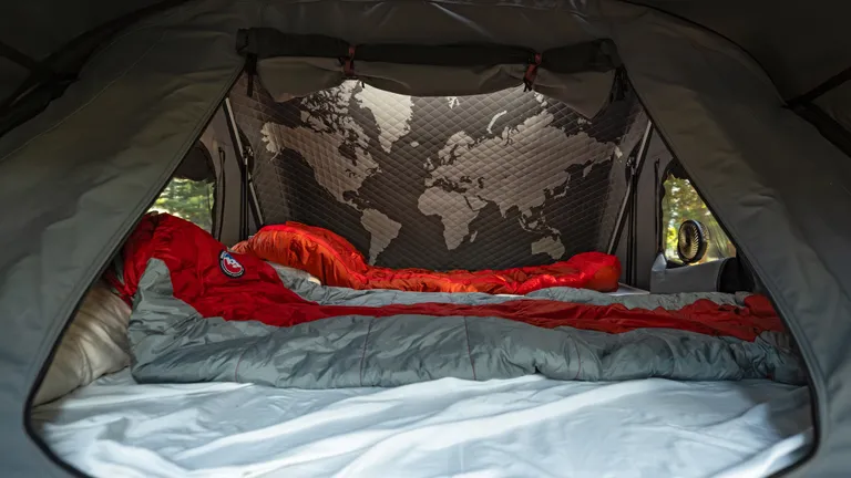 A vehicle with the iKamper Skycamp DLX rooftop tent parked by a lake at sunset