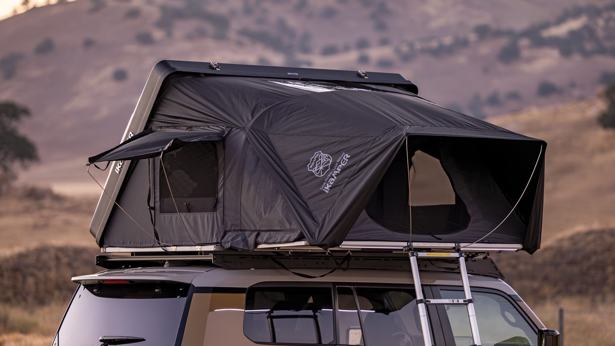 The iKamper Skycamp DLX rooftop tent deployed on a vehicle amidst a scenic natural backdrop