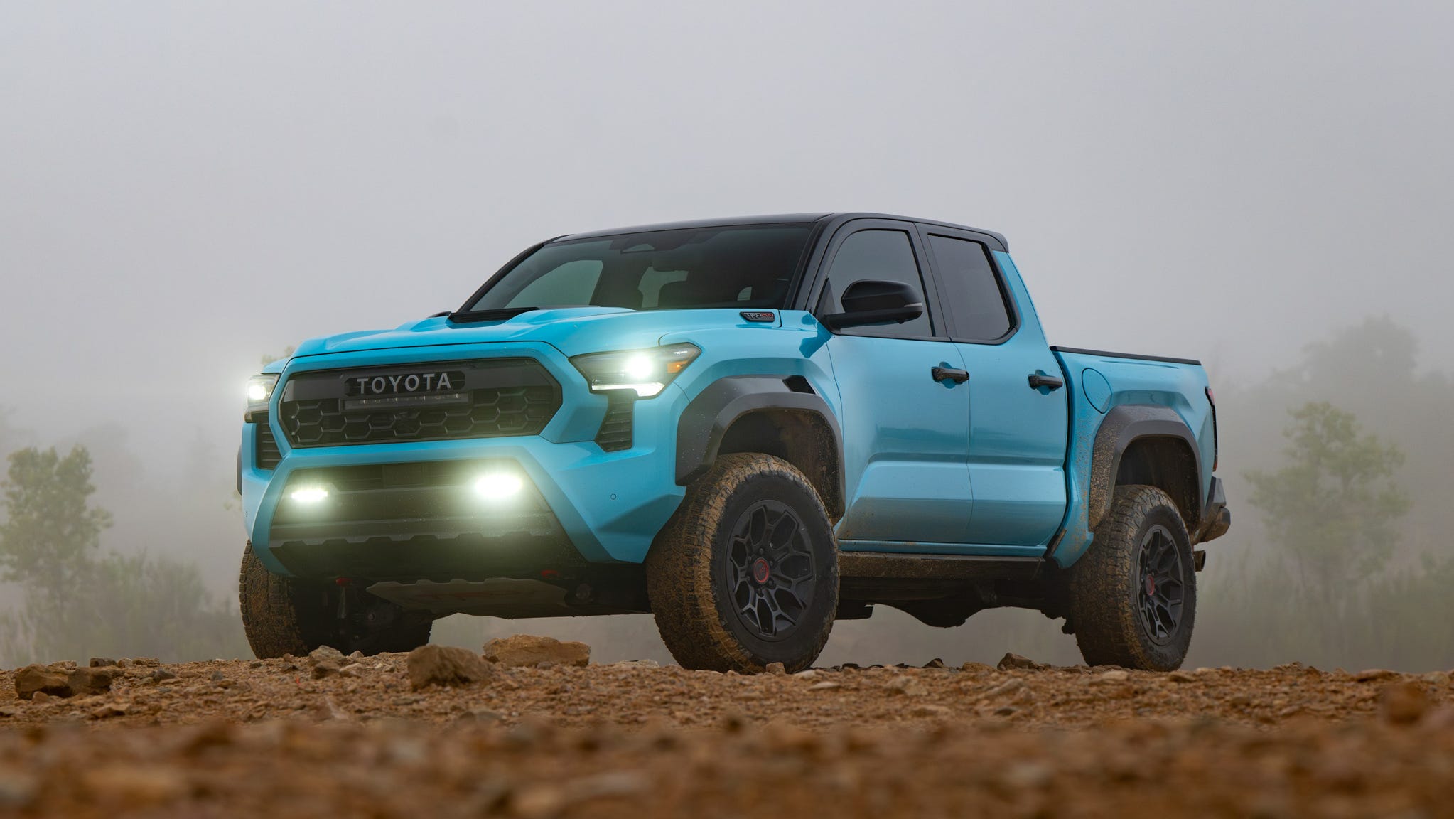 A rugged Toyota Tacoma navigating an unpaved, dusty trail, highlighting its off-road capabilities and durable construction.